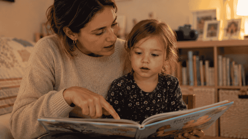 A preschool-age child looking at a picture book with a parent, showing early language engagement that parents can observe