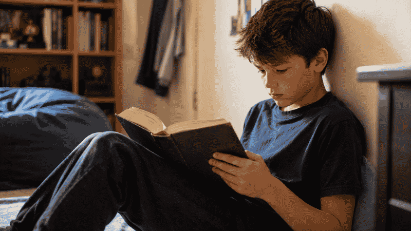 An 11-year-old deeply absorbed in a thick fantasy novel, leaning against a wall with complete focus and intensity