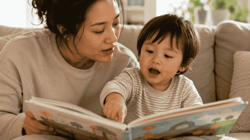 A parent and 2-year-old toddler in conversation during a picture book read-aloud, the child pointing and the parent listening