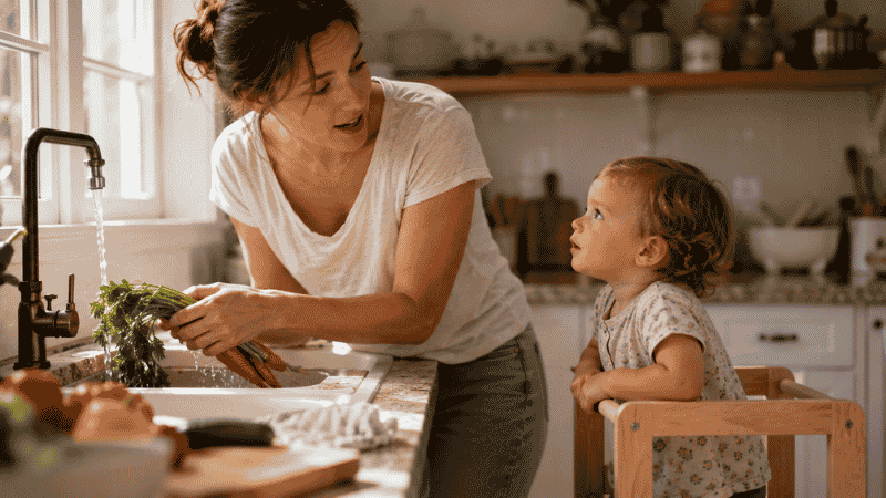 A parent narrating a daily routine to a toddler in the kitchen, building vocabulary through everyday conversation