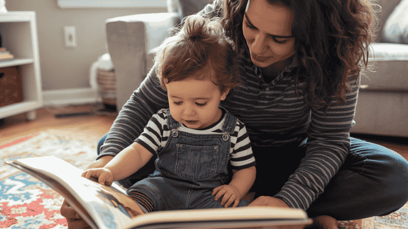 A parent and a 3-year-old child sitting together on a colorful play rug, deeply engaged in an oversized picture book with expressive, happy faces, illustrating active storytime participation.