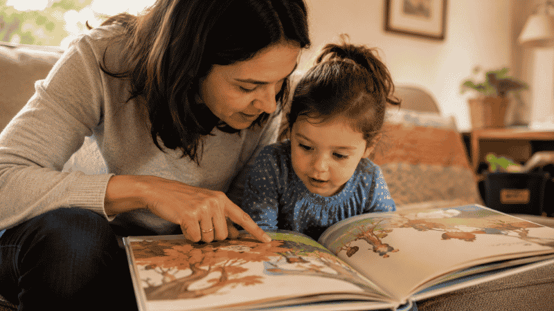 A parent and young child looking closely at the illustrations in an award-winning picture book together, both engaged with what the pictures show