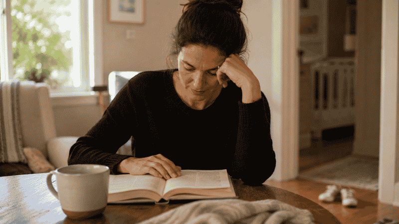 A parent reading a parenting book during a quiet moment while their toddler naps, taking notes with genuine focus